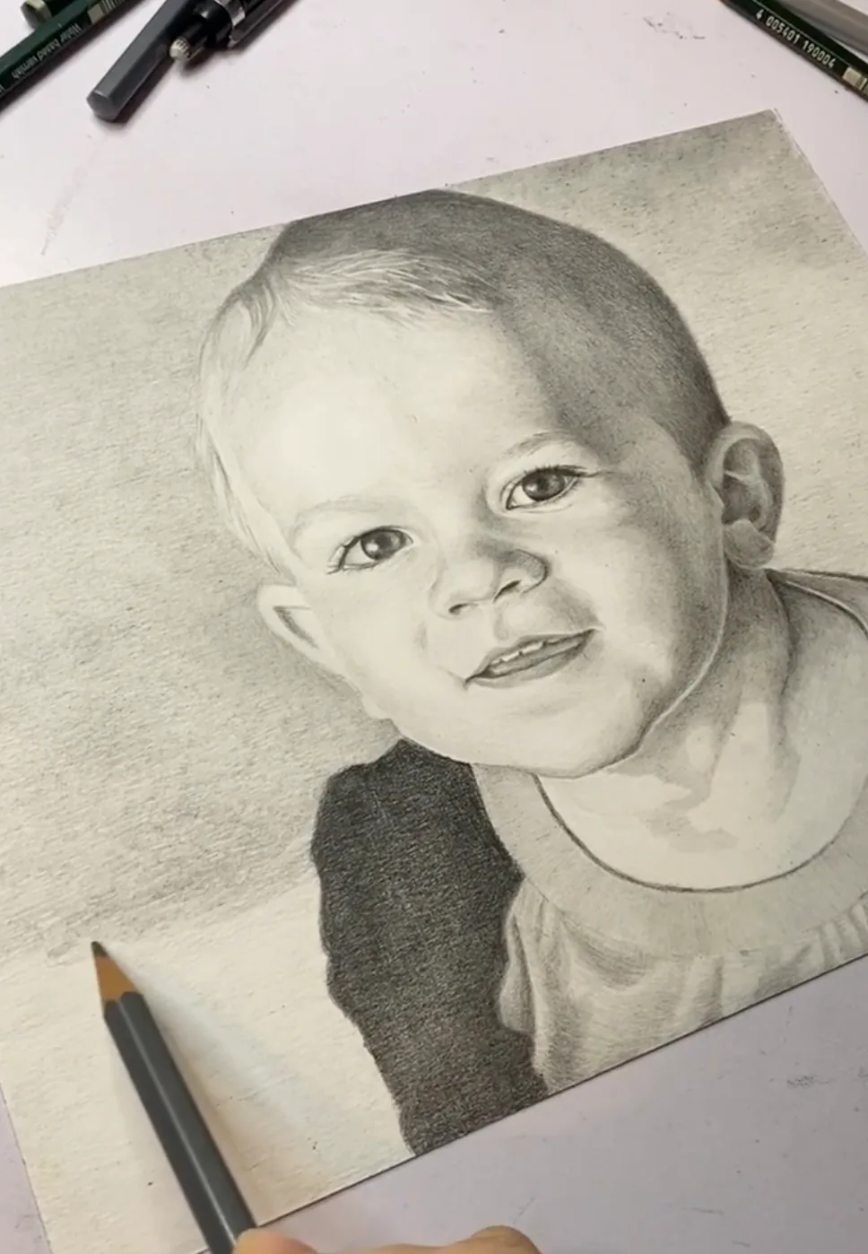 Graphite portrait of a smiling baby in progress